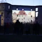Ludzie oglądający wieczorny pokaz mappingu na murach Zamku w Janowcu