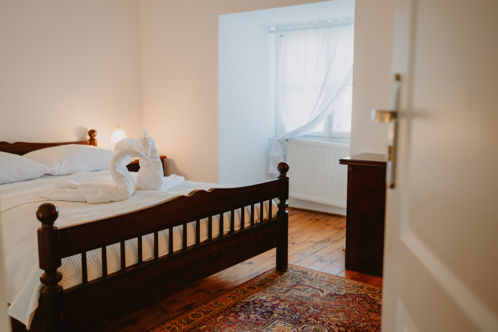 Na wpół otwarte drzwi, łóżko małżeńskie, na łóżku dwa ręczniki złożone na kształt łabędzi.