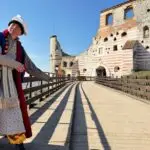 Pracownik muzeum w kostiumie nawiązującym do stylu sarmatyzmu przed Zamkiem w Janowcu zapraszający do zwiedzania muzeum